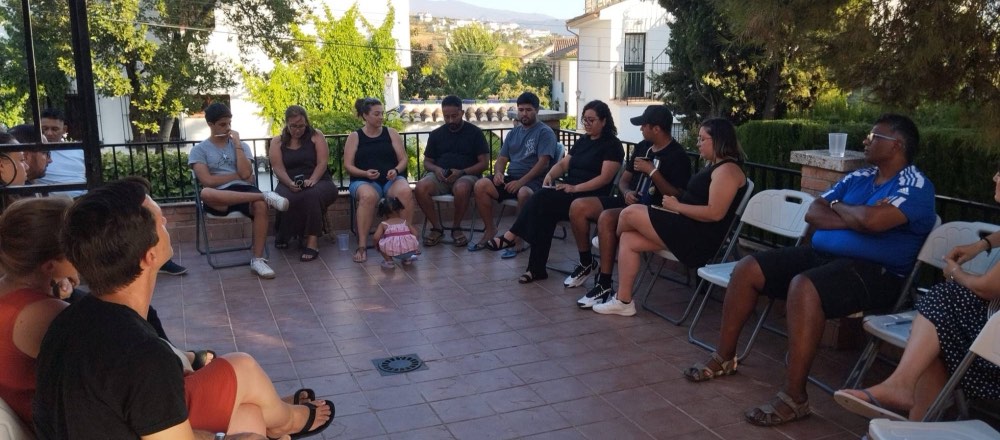 Un círculo de personas orando juntas en una terraza al atardecer