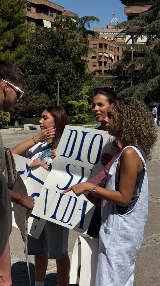 Estudiantes con carteles pintados a mano hablando con un joven en una plaza de Granada